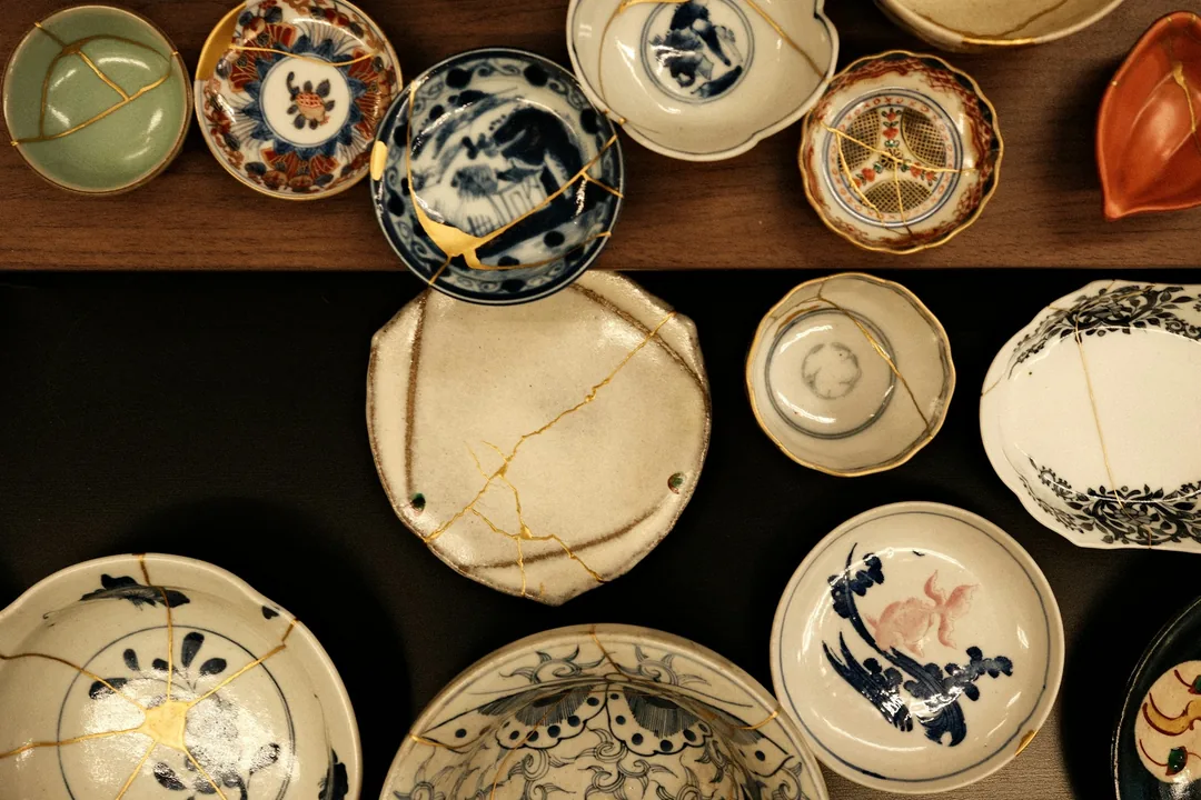 Několik keramických misek a talířů opravených metodou kintsugi, spoje jsou zvýrazněné zlatou linkou.